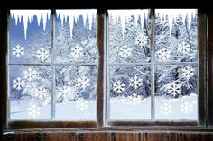 a window with snowflakes on the outside and inside, in front of a snowy forest