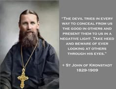 a man with a long beard wearing a gold cross necklace and black shirt, sitting in front of a gray background