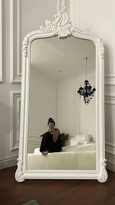 a woman taking a selfie in front of a large white mirror with a chandelier hanging from the ceiling