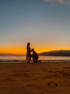 two people sitting on the beach at sunset