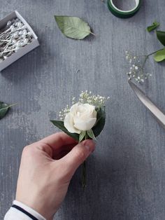 someone is holding a white flower in their left hand and some scissors on the table