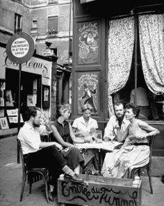 four people sitting at a table in front of a store with writing on the side