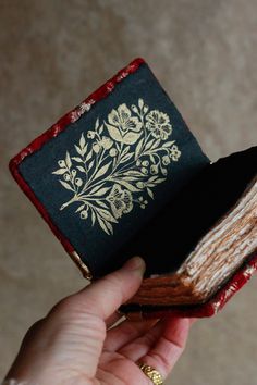 a person holding an open book in their left hand and the cover is black with white flowers on it