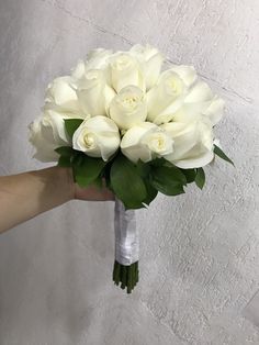 a bouquet of white roses is held by a person's hand in front of a wall