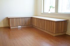 an empty room with wood flooring and a bench in front of a large window