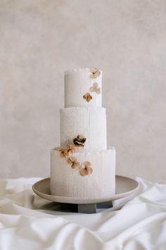 a three tiered white cake with flowers on it sitting on a plate in front of a wall