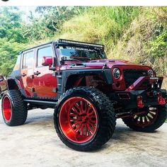 a red jeep parked in front of a lush green hillside