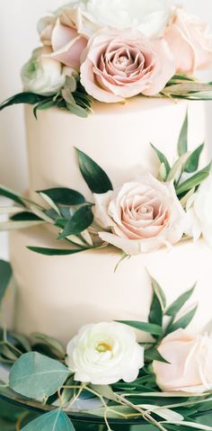 a three tiered wedding cake with pink and white flowers on the top, surrounded by greenery