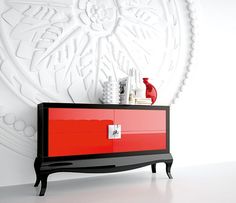 a red and black dresser in front of a white wall with an intricate design on it