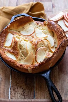 an apple pie in a cast iron skillet on a wooden table next to sliced apples