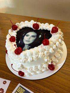 a white cake with cherries on it sitting on a table next to a book