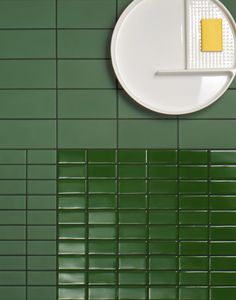 a green tiled wall with a white plate and yellow object on it's side