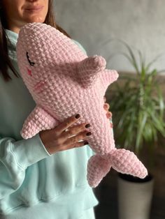 a woman holding a pink crocheted cat stuffed animal