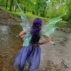 a woman with purple hair and blue wings is standing in the water near a stream