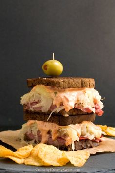 two sandwiches stacked on top of each other with chips and an olive in the background