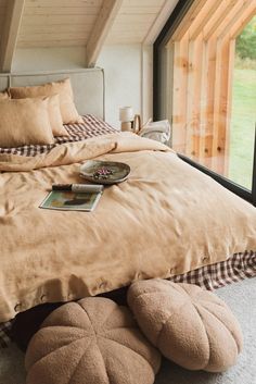 a bed with pillows and blankets on it in a bedroom next to a large window