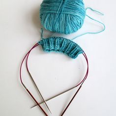 two skeins of yarn next to each other with knitting needles in the foreground