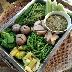 an assortment of vegetables and dip in a metal tray on a wicker table outdoors