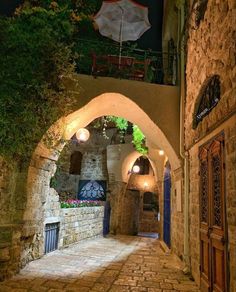 an alley way with stone walls and arched doorways, lit by lights at night