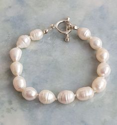 "7\" silver plated white freshwater pearl bracelet.  Rice shape white freshwater pearl approximately 9.5mm - 10.5mm finished with a silver plated toggle clasp. Hand knotted between each pearl, with good quality natural silk thread.  The pearls are genuine freshwater pearls therefore each pearl is slightly different in shape and size and each pearls has it own unique natural blemishes.  The colour of the actual bracelet might be slightly different to the photo due to the lighting  All measurement White Baroque Pearl Bracelets For Formal Occasions, Formal White Baroque Pearl Bracelets, Silver Baroque Pearl Bracelets With Round Beads, Silver Bracelet With Baroque Pearls, Adjustable White Baroque Pearl Bracelet, Formal White Baroque Pearl Bracelet, Classic Silver Pearl Bracelet With Pearl Drop, Silver Baroque Pearl Bracelet With Round Beads, Classic Silver Pearl Drop Bracelet