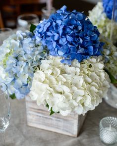 blue and white hydrangeas in a wooden box on a table with wine glasses