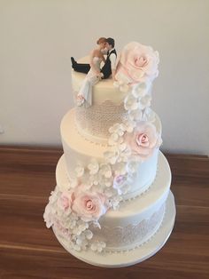 a white wedding cake with pink flowers and a bride and groom sitting on the top