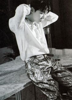 a man sitting on top of a counter next to a table with his hands behind his head