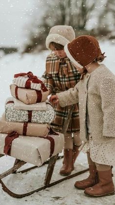 two children pulling a sleigh with presents on it in the snow and one child is wearing a hat