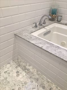 a white bathroom with marble counter tops and tile flooring on the walls, along with a bathtub