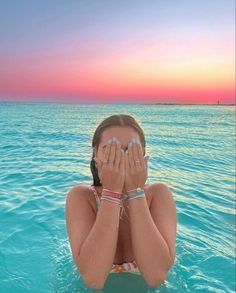 a woman covers her eyes while floating in the ocean at sunset or dawn with both hands on her face