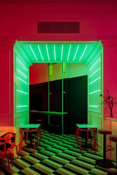 an empty room with tables and stools lit up by neon lights in the doorway