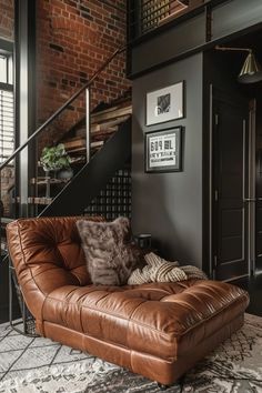 a brown leather couch sitting in front of a stair case next to a brick wall