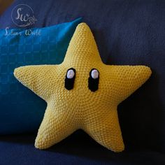 a yellow knitted starfish with eyes sitting next to a blue pillow on a bed