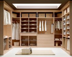 a walk in closet filled with lots of wooden shelves and white clothes on hangers