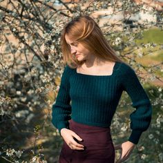 a woman standing in front of a tree with her hands on her hips, wearing a green sweater