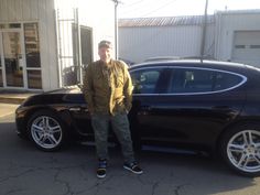 a man standing next to a black sports car in front of a building with white doors