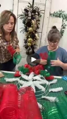 two women are making christmas decorations at a table with red and green ribbons on it