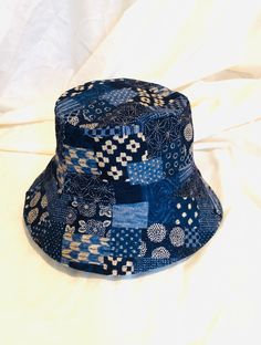 a blue and white patterned hat sitting on top of a white cloth covered bed sheet