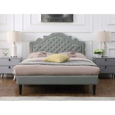 a bed with a gray headboard and two lamps on either side of the bed