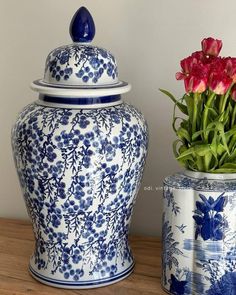 two blue and white vases with flowers in them sitting on a table next to each other