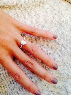 a woman's hand with a diamond ring on top of her left hand, resting on a blanket