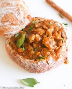 two breads with meat and vegetables are on a white surface next to cinnamon sticks