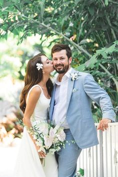 a bride and groom kissing in front of a white fence with greenery behind them