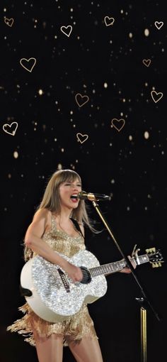 the singer is singing into her microphone and holding an acoustic guitar in front of hearts