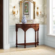 a table with a mirror and vase on it in front of a wallpapered room