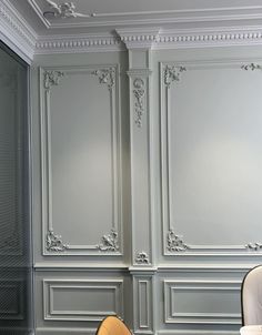 a white chair sitting in front of a gray wall with ornate carvings on the walls