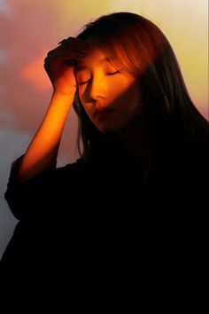 a woman is holding her head in front of the camera with an orange light behind her