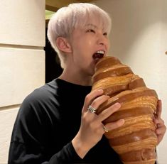 a person with white hair holding a large pastry in front of their face and biting into it