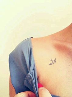 a woman with a small bird tattoo on her chest and shoulder, holding onto the arm