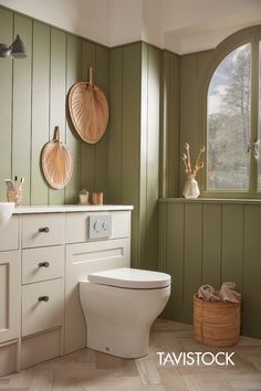 a white toilet sitting next to a window in a green room with wood paneling